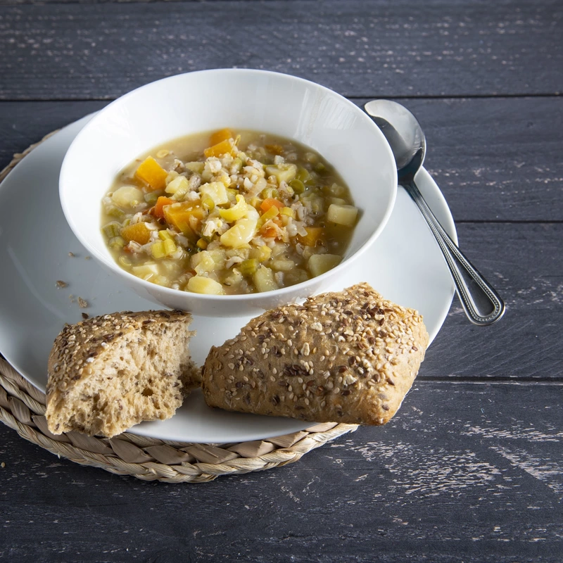 A bowl of country vegetable soup with a crusty roll