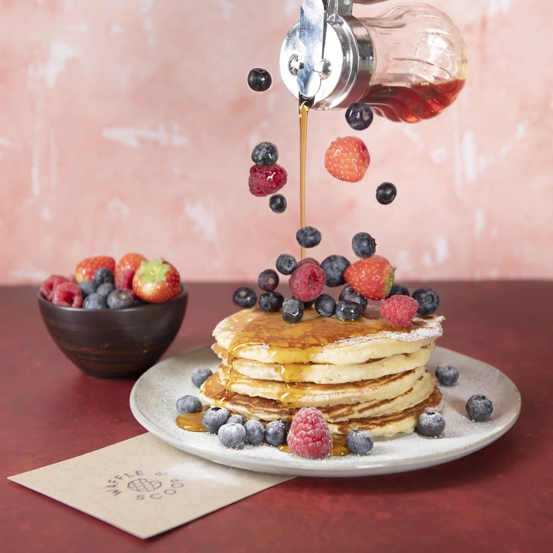 Syrup and fresh berries being poured over a plate of pancakes