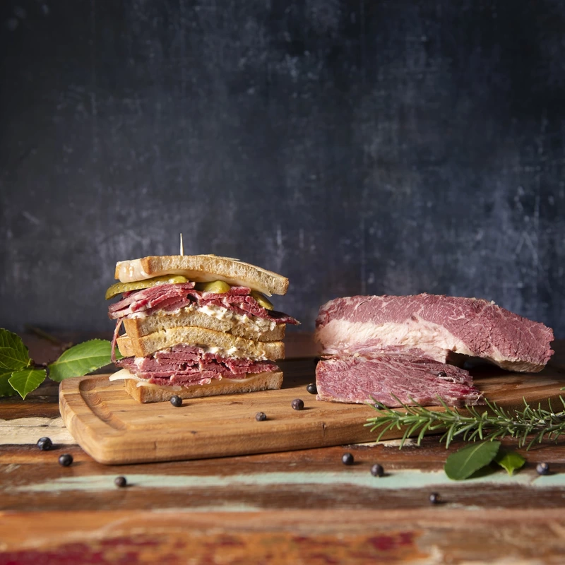 Salt beef sandwich with gherkins next to a cut of salt beef