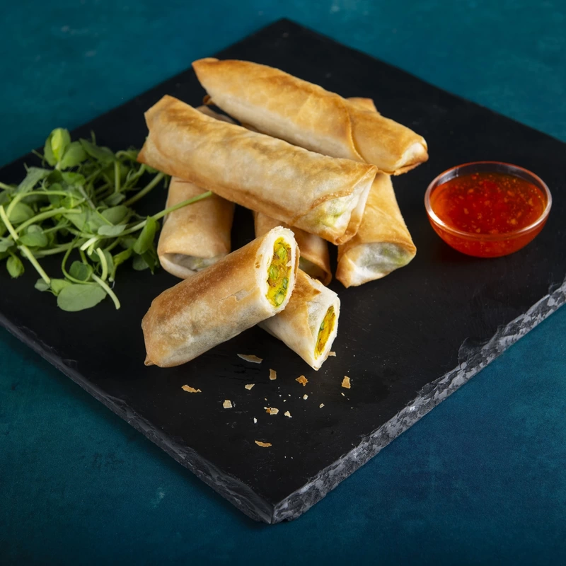 Vegetable spring rolls on a slate with garnish and sweet chilli sauce